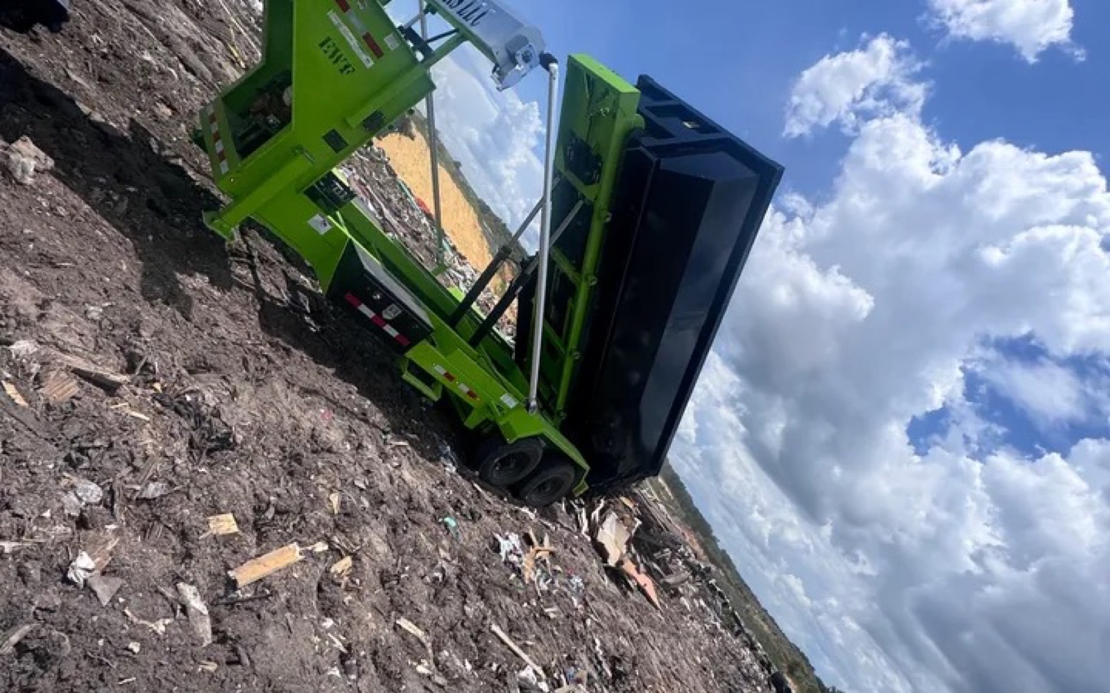 DJ's Dumpsters equipment unloading a black roll-off container at a debris disposal site