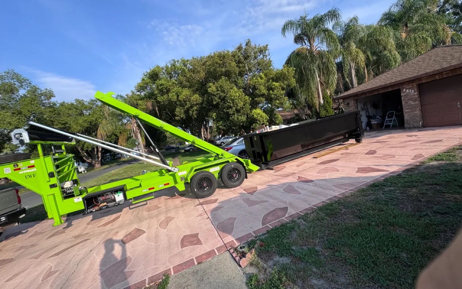 DJ's Dumpsters roll-off trailer placing a black dumpster on a Central Florida driveway