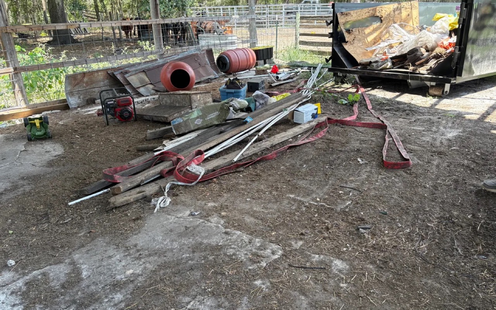 Outdoor property cleanup with yard and project debris beside a black roll-off dumpster