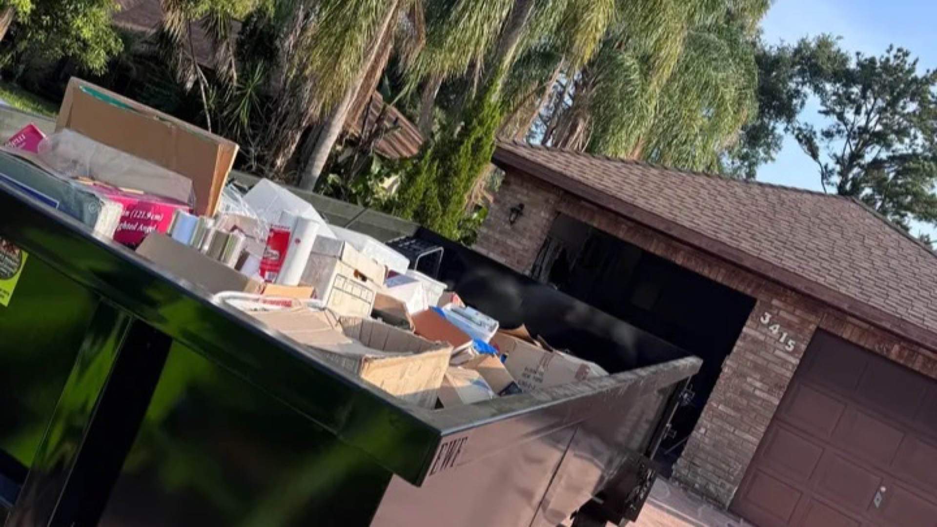 Black roll-off dumpster loaded with household boxes on a residential driveway