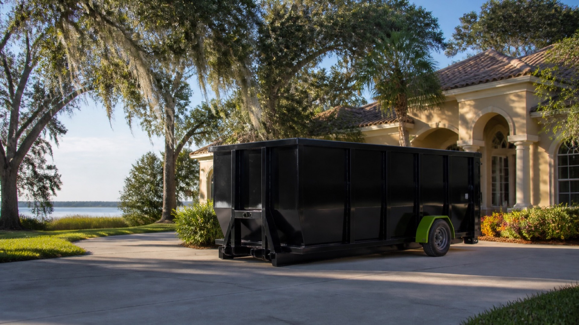 Black roll-off dumpster on a Tavares-area driveway beside a lake and mature trees
