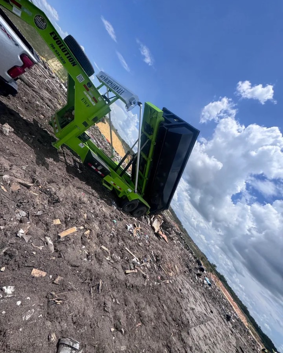 Black roll-off container being unloaded from lime-green trailer equipment