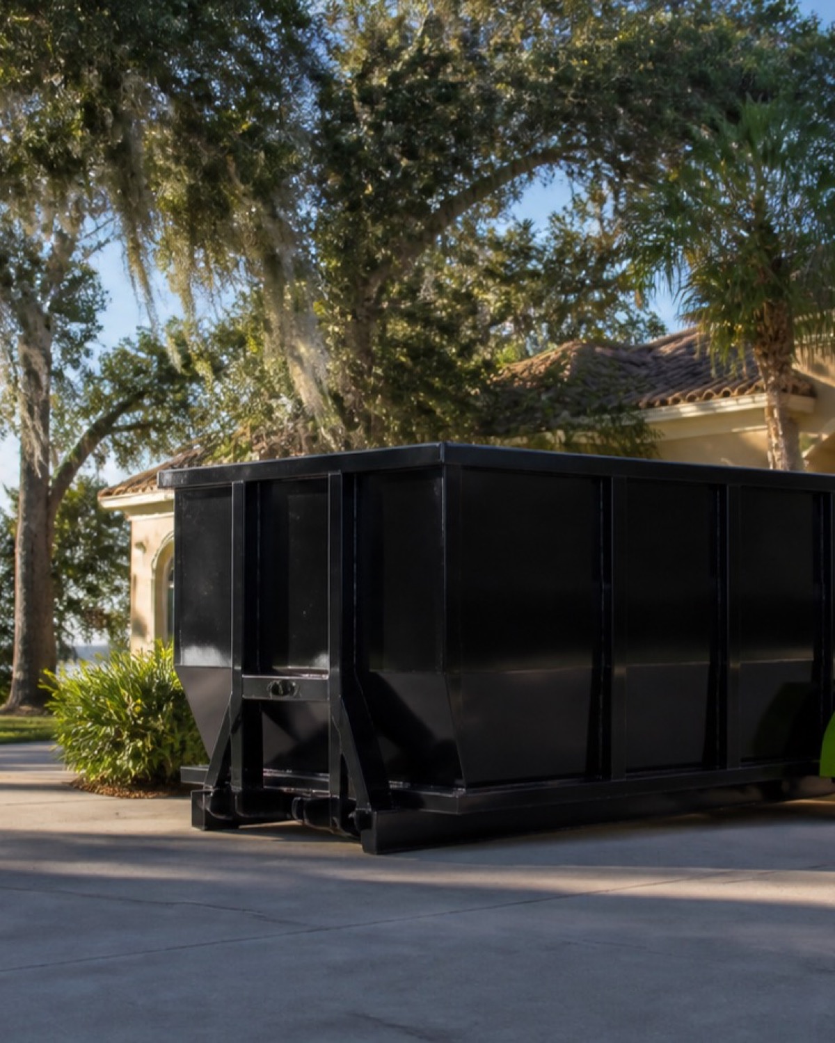 Unbranded black roll-off container on a landscaped lake-region driveway in Tavares